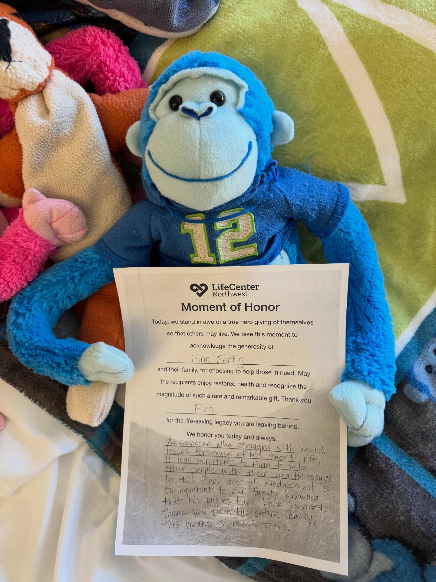 Finn's blue monkey holding a LifeCenter Northwest Moment of Honor certificate
